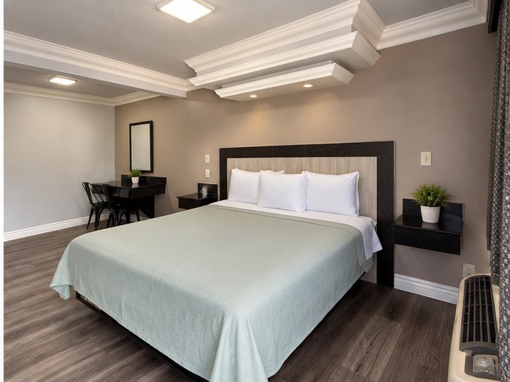 King room with a green bedspread, dark headboard and a desk in the corner