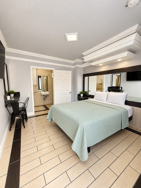 Queen room with a soft green bedspread and tiled floor.
